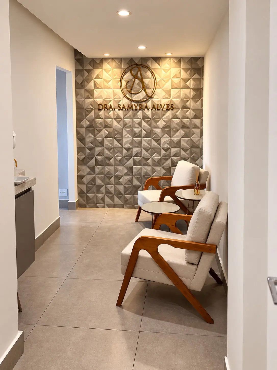 Ambiente acolhedor da recepção do consultório da Dra. Samyra Alves, com duas poltronas claras, mesinhas de centro e cantinho do café para maior conforto dos pacientes.